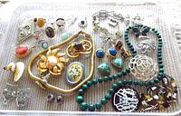 Top view of assorted vintage jewelry laid out on a flat surface including necklaces, rings, brooches, and earrings.