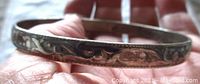 Close-up of silver embossed detail on the bangle showing swirling floral or scroll pattern with patina.