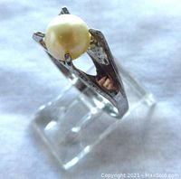 Front angled view showing the pearl set in claw-style sterling silver band on a display stand.