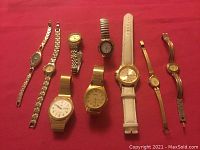 Eight vintage watches arranged side by side on red fabric background. Watches vary in size, strap type, and dial design.