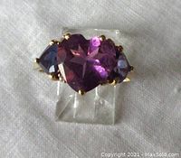 Front view of ring on clear stand showing heart-shaped amethyst and side sapphires