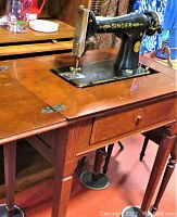 Singer sewing machine mounted in open wood cabinet stand showing the front drawer and side panel with foot pedal below.