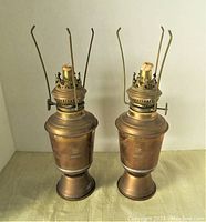 Pair of two Nakamura signed brass or bronze oil lamps shown side by side with visible wicks, 12 inches tall