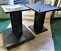 Two black stereo speaker stands with square base and top and carpet spikes visible on top platforms.
