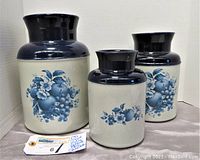 Set of three McCoy pottery canisters showing front floral designs in blue on white ceramic with dark blue rims.