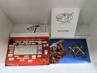 Photo showing white NOX Reference Guide booklet, keyboard controls layout card, and cover artwork card with warrior and NOX logo