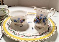 Open sugar bowl and creamer sitting on the 11-inch Nantucket snack plate with floral and gold rim design