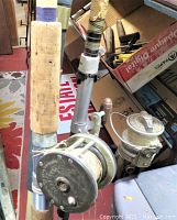 Close-up of the cork handle and reel attached to the fishing pole showing worn cork grip and vintage round metal casting reel with fishing line.