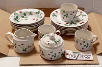 Photo showing entire set with cups, bowls, plates, sugar bowl with lid, and creamer all decorated with strawberry and green leaf pattern on white ceramic.