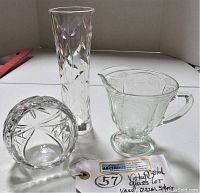 Front and top view of the cut crystal orb, etched glass creamer, and crystal vase arranged on a white surface with a red ruler for size reference and auction tag.
