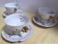 Three vintage fine china teacups each with a different shaped base, floral pattern, and matching saucer. Teacups have gold rim and handles.