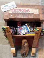Open wooden SHINOLA shoe shine box showing shoe polish, brushes, and Speed Wax bottle inside with attached RITZ shoe sizers hanging on the front.