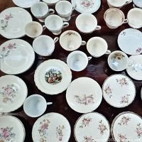 Top down view of assorted vintage teacups, saucers, and plates arranged on a wooden surface showing floral and gold rim designs.