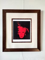 Front view of the framed Andy Warhol lithograph showing the red-on-black self-portrait with the wooden frame and cream mat.