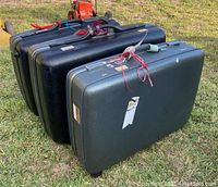 Side view of three vintage American Tourister hard case suitcases stacked on grass showing their hard shell and wear.
