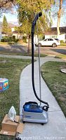 Photo showing the full setup of SteamFast Professional clothes steamer with stand and hose, along with a white Sunbeam iron placed on its box on the ground.