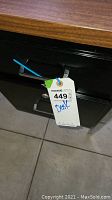 Close-up photo of desk drawer lock tag attached, showing metal drawer front and wood top edge.