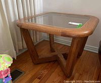 Side angle photo showing solid wood base with angled legs and square glass top with brass trim.