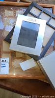 Various picture frames placed overlapping on table including light wood multi-photo frame and silver metal frame, black multi-slot frame, and boxed set
