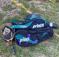 Three Prince branded tennis racket cases on grass, one with a Prince tennis racket inside, showing logos and color accents.
