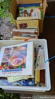 Box and bin filled with various cookbooks and gardening books, showing a diverse collection of titles and subjects.