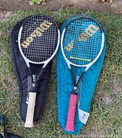 Photo of two Wilson tennis rackets side by side on grass, one with white grip and black case, the other with pink grip and blue case