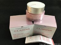 Two jars of Clarins Multi-Active Day Cream with two original boxes on black background. One cream jar open, showing cream inside.