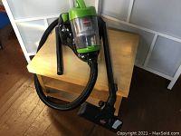 Full vacuum cleaner unit placed on a wooden table showing the canister with hose and floor brush attachment.