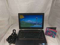 Image showing Dell Latitude E6420 laptop powered on with Windows 8 lock screen and included Windows 8 Pro install disk next to it alongside charger cables.
