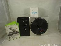 The DJ Hero 2 game case, Xbox 360 controller, and DJ Hero 2 turntable controller. Shows physical condition and size comparison.