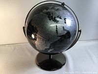 Black metallic world globe on polished black stand showing Africa and parts of Europe, with reflective surface and silver continent outlines.