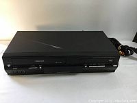 Front view of Toshiba DVD VCR combo deck showing DVD slot, VHS tape slot, AV inputs, and control buttons under good lighting conditions on white background.