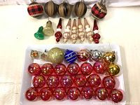 Photo showing a variety of Christmas ornaments including red balls, fabric-covered balls, gold and brown ribbed balls, and different shaped glass ornaments.