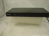 Front angle view of the black Samsung BDE5300 Blu-ray player showing the disc tray and front panel controls.