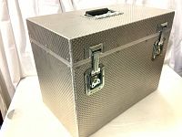 Closed aluminum trunk showing textured surface, two key lock latches and a black handle on top.