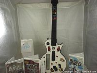 White Wii guitar controller decorated with red stars and music stickers standing upright next to game cases including Rock Band 2 and The Beatles Rock Band