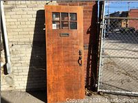 Full view of rusty brown solid oak front door leaning against wall, shows mailbox slot and hardware on right