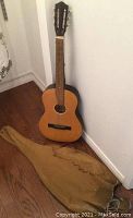 Full view of acoustic guitar standing against a wall with cotton carrying bag on floor