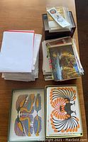Top view showing stacks of assorted cards and postcards, with visible seasonal and message variety, including two large card designs featuring stylized birds in orange, black, and grey.