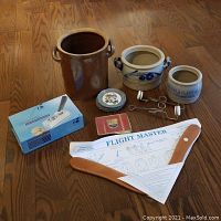 Photo showing the full assortment of items on wooden floor, including ceramic crocks, cherry pitters, coasters, nutcracker, cigarette tin, and boomerang with instructions.