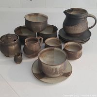Image showing entire pottery set arranged on white surface including bowls, pitchers, creamer, sugar bowl, and plates in brown and cream earth tones.