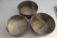 Three earth tone pottery bowls grouped on white surface, showing inside and outside glaze in brown and cream.