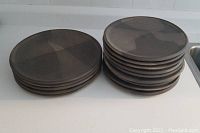 Two stacks of pottery plates on a countertop showing 5 larger and 9 smaller plates