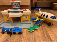Fisher Price airport building with control tower and two Fisher Price airplanes, plus additional vehicles, showing overall set contents on wood floor