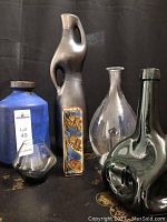 Group photo of five vases in different materials and styles on a black patterned surface with black background.