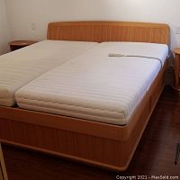 Full view of light wood finish king size adjustable bed frame with two mattresses and curved headboard.
