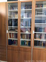 Front view of large six shelf glass door wood cabinet filled with books