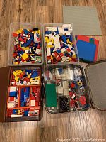 Two clear plastic totes filled with assorted primary-colored LEGO bricks next to stack of small plates and a large gray baseplate