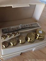 OHAUS brass weights in white plastic tray, showing 9 weights with value markings
