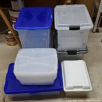 Photo showing the mix of plastic totes including large clear totes with blue lids, a small white storage bin, and nested long shallow white bins stacked on top of a large blue-lid plastic tote